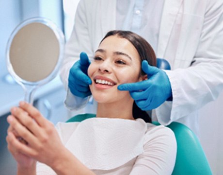 Woman smiling while looking at teeth in handheld mirror