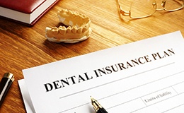 Dental insurance form next to glasses and model of teeth