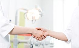 Dentist and patient shaking hands in front of dental chair