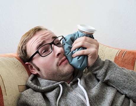 man holding a cold compress to his cheek after getting tooth extractions in Gainesville 