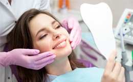 Woman checking smile in mirror after getting dental implants in Gainesville, GA