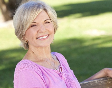 Senior woman with implant dentures sitting outside on park bench