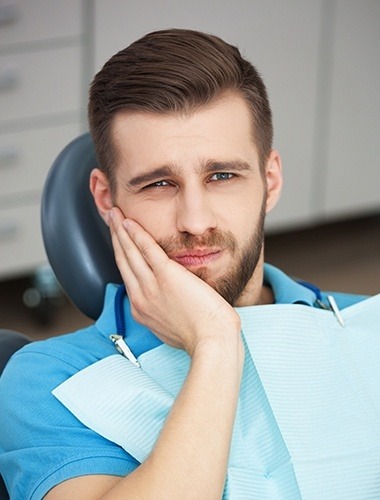 Man holding cheek in pain in dental chair