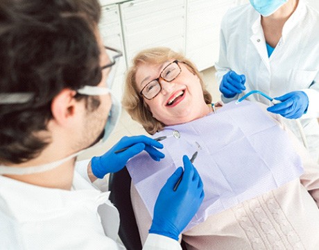 Woman with glasses smiling at dentist while sitting in treatment chair