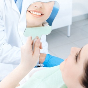 Dental patient using mirror to admire results of her cosmetic treatment