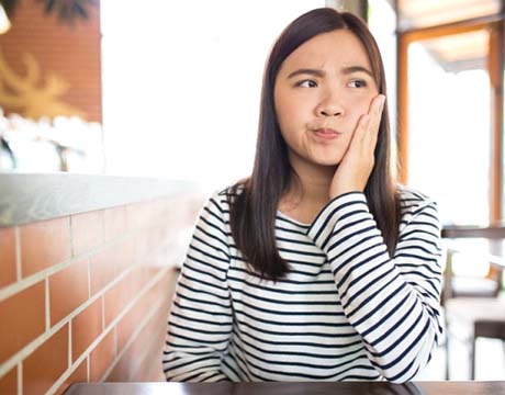 Woman in café wondering if she should call her Gainesville emergency dentist