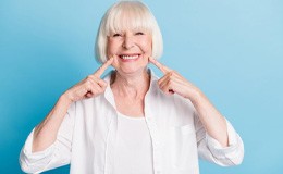 a woman smiling and pointing at her new dentures